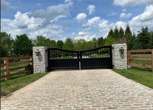 Arched black iron estate gate with stone columns and cobblestone drive
