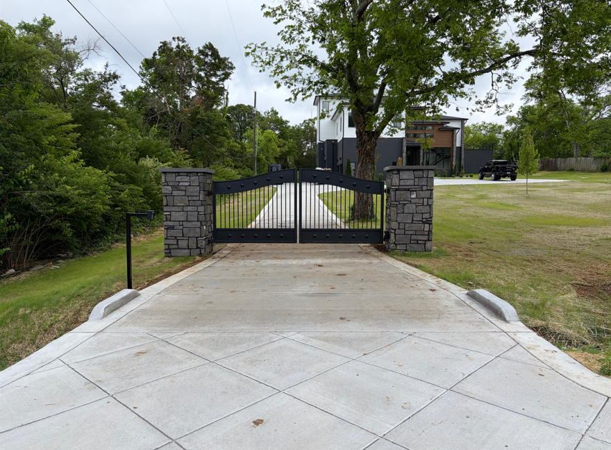 Black arched iron driveway gate with stacked stone columns