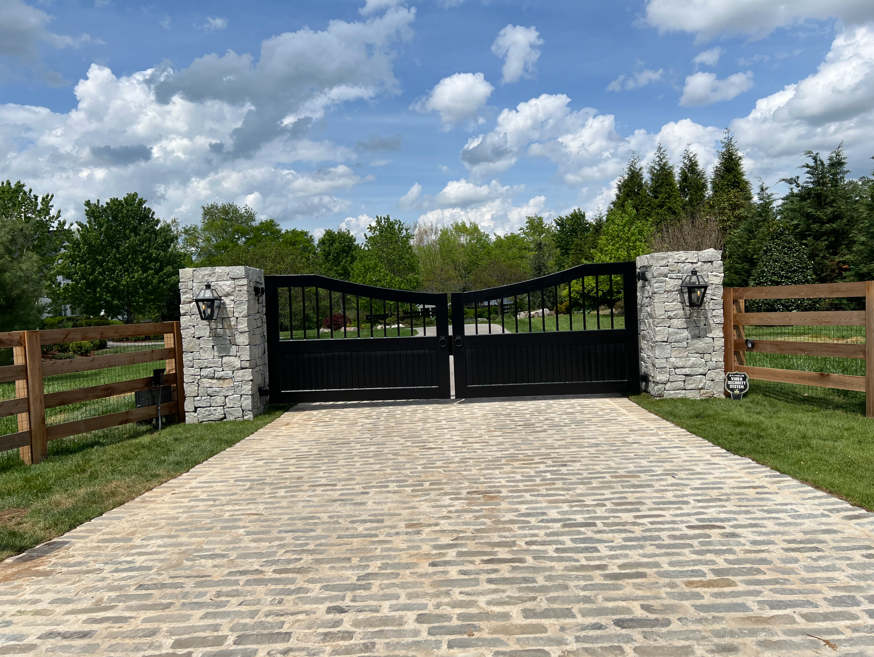 Black solid-panel arched estate gate with stone columns and lanterns