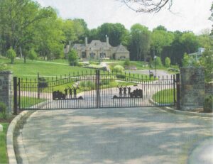 A gated driveway with trees and houses in the background.